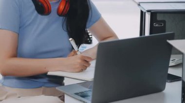 Evde dizüstü bilgisayar ve defter kullanan genç bir kadın.