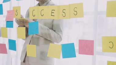 Genç iş kadını ofiste dururken cam tahtaya yazı yazıyor.