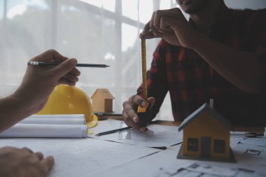 İnşaat mühendisi Asyalı 'nın ofis masasındaki inşaat sahasında mimari tasarım projesi üzerinde çalışmasını kapatın..