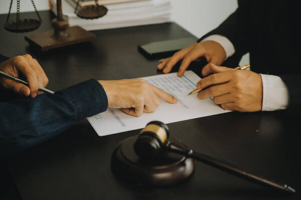 Понятие правосудия и права. Юридический консультант представляет клиенту подписанный договор с молотком и юридическим правом или проведение группового заседания в юридической фирме на заднем плане
