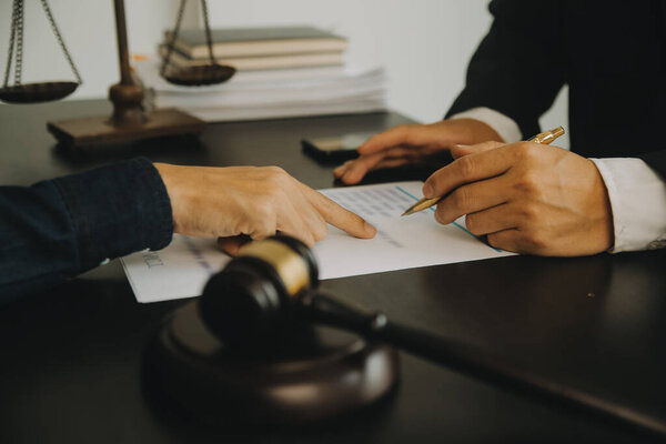 Понятие правосудия и права. Юридический консультант представляет клиенту подписанный договор с молотком и юридическим правом или проведение группового заседания в юридической фирме на заднем плане
