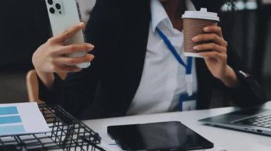 Ofiste akıllı telefon ve laptop kullanan genç bir iş kadını.