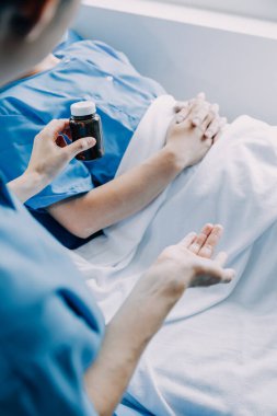 Hastanede koğuşta yatakta Asyalı kadın hasta muayene çeşitli doktorların yan görünümü.