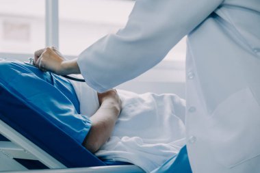 Hastanede koğuşta yatakta Asyalı kadın hasta muayene çeşitli doktorların yan görünümü.