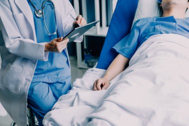 Hastanede koğuşta yatakta Asyalı kadın hasta muayene çeşitli doktorların yan görünümü.