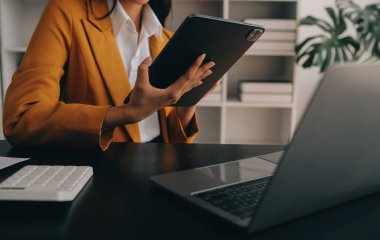 Çekici gülümseyen Asyalı iş kadını ev ofisinde çalışıyor, Asyalı kadın dizüstü bilgisayarında tablet tutuyor..