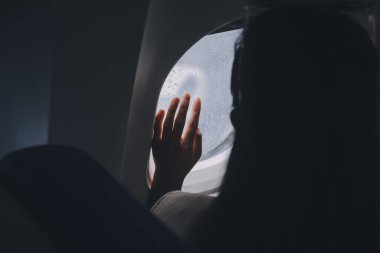 Kadın silueti uçan bir uçağın penceresinden dışarı bakar. Uçağın yolcusu pencerenin yanında dinleniyor..