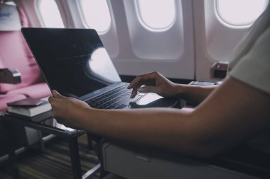 Pencerenin yanında uçakta oturan ve sosyal ağlardan haber okuyan veya akıllı telefonda seyahat uygulamalarını kullanan Asyalı kadın yolcu