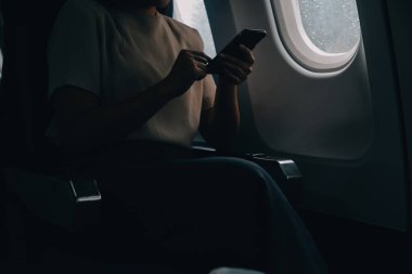 Çekici Asyalı kadın uçak yolcusu dizüstü bilgisayar ve tabletle kablosuz bağlantı kullanarak rahat koltukta oturuyor. Stil içinde seyahat et, zarafetle çalış..