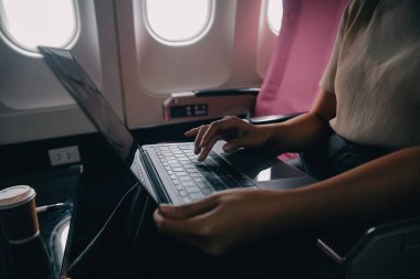 Pencerenin yanında uçakta oturan ve sosyal ağlardan haber okuyan veya akıllı telefonda seyahat uygulamalarını kullanan Asyalı kadın yolcu