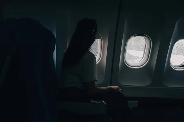 一个女人的轮廓从一架飞行的飞机的窗户向外张望 飞机上的乘客在窗边休息 — 图库照片