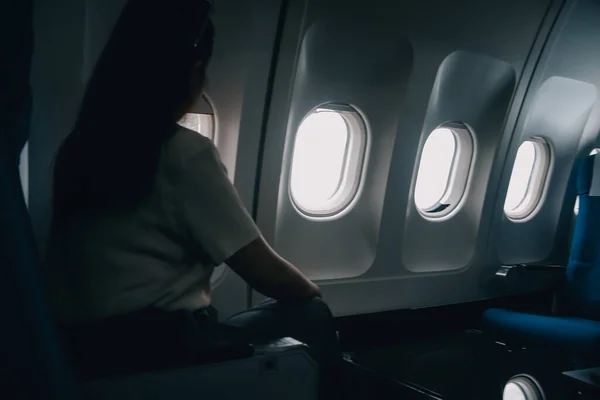 Silhouette of woman looks out the window of an flying airplane. Passenger on the plane resting beside the window.