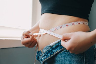Şişman kadın, şişko, obez kadın el ele tutuşan ölçü bandıyla göbek yağı, kadın diyeti yaşam tarzı konsepti