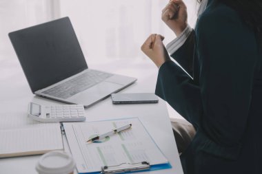 İş kadını dizüstü bilgisayarda çalışırken cep telefonu kullanıyor, internette sörf yapıyor, modern ofiste iş verilerini araştırıyor. İş yerinde bilgisayarla çalışan Asyalı iş kadını