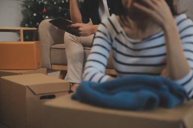 İki Asyalı blogcu, dükkanında canlı yayın yapan videoyu kaydetmek için kameranın önünde kıyafetlerini gösteriyor. Çevrimiçi alışveriş arabası fikri. Evdeki kanepede.