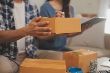 İki Asyalı blogcu, dükkanında canlı yayın yapan videoyu kaydetmek için kameranın önünde kıyafetlerini gösteriyor. Çevrimiçi alışveriş arabası fikri. Evdeki kanepede.