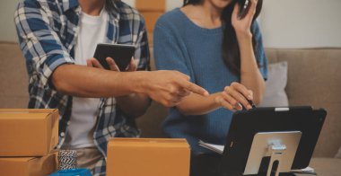 İki Asyalı blogcu, dükkanında canlı yayın yapan videoyu kaydetmek için kameranın önünde kıyafetlerini gösteriyor. Çevrimiçi alışveriş arabası fikri. Evdeki kanepede.