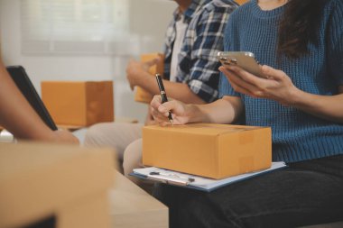 İki Asyalı blogcu, dükkanında canlı yayın yapan videoyu kaydetmek için kameranın önünde kıyafetlerini gösteriyor. Çevrimiçi alışveriş arabası fikri. Evdeki kanepede.