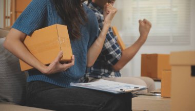 İki Asyalı blogcu, dükkanında canlı yayın yapan videoyu kaydetmek için kameranın önünde kıyafetlerini gösteriyor. Çevrimiçi alışveriş arabası fikri. Evdeki kanepede.