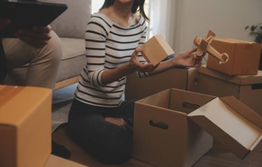 İki Asyalı blogcu, dükkanında canlı yayın yapan videoyu kaydetmek için kameranın önünde kıyafetlerini gösteriyor. Çevrimiçi alışveriş arabası fikri. Evdeki kanepede.