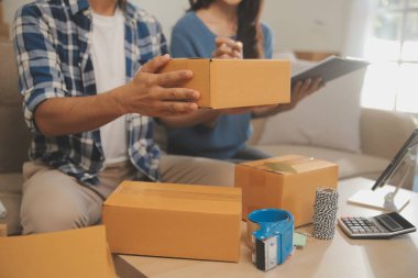 İki Asyalı blogcu, dükkanında canlı yayın yapan videoyu kaydetmek için kameranın önünde kıyafetlerini gösteriyor. Çevrimiçi alışveriş arabası fikri. Evdeki kanepede.