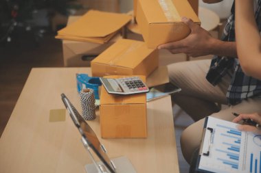 İki Asyalı blogcu, dükkanında canlı yayın yapan videoyu kaydetmek için kameranın önünde kıyafetlerini gösteriyor. Çevrimiçi alışveriş arabası fikri. Evdeki kanepede.