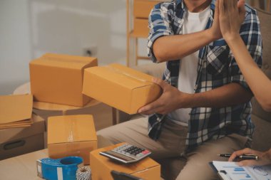 İki Asyalı blogcu, dükkanında canlı yayın yapan videoyu kaydetmek için kameranın önünde kıyafetlerini gösteriyor. Çevrimiçi alışveriş arabası fikri. Evdeki kanepede.