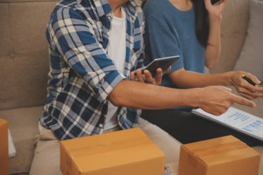 İki Asyalı blogcu, dükkanında canlı yayın yapan videoyu kaydetmek için kameranın önünde kıyafetlerini gösteriyor. Çevrimiçi alışveriş arabası fikri. Evdeki kanepede.