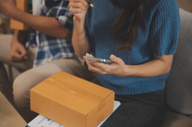 İki Asyalı blogcu, dükkanında canlı yayın yapan videoyu kaydetmek için kameranın önünde kıyafetlerini gösteriyor. Çevrimiçi alışveriş arabası fikri. Evdeki kanepede.