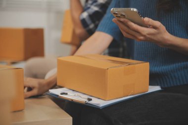 İki Asyalı blogcu, dükkanında canlı yayın yapan videoyu kaydetmek için kameranın önünde kıyafetlerini gösteriyor. Çevrimiçi alışveriş arabası fikri. Evdeki kanepede.