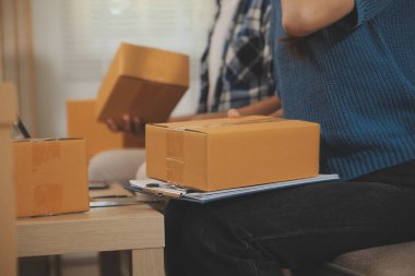 İki Asyalı blogcu, dükkanında canlı yayın yapan videoyu kaydetmek için kameranın önünde kıyafetlerini gösteriyor. Çevrimiçi alışveriş arabası fikri. Evdeki kanepede.