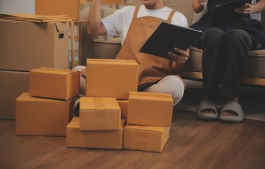 İki Asyalı blogcu, dükkanında canlı yayın yapan videoyu kaydetmek için kameranın önünde kıyafetlerini gösteriyor. Çevrimiçi alışveriş arabası fikri. Evdeki kanepede.