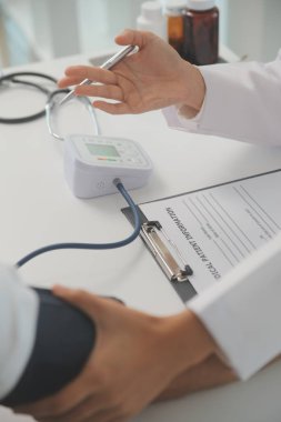 Erkek doktor, check-up, tıbbi tedavi ve sağlık konsepti için hastaneye gelen hastaların vücut basıncını ve nabzını ölçmek için kan basıncı monitörü kullanır..