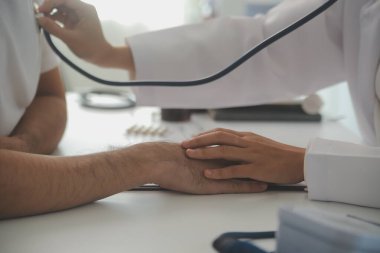 Genç doktor steteskop kullanıyor. Hastanın kalp atışlarını dinle. Kadın bir doktorun erkek bir hastaya muayene yaparken görüntüsü.