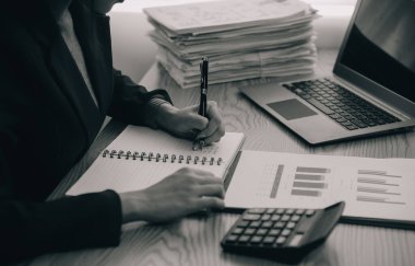 Asyalı iş kadını dizüstü bilgisayar kullanıyor ve ofiste hesap makinesi ile çalışıyor, mali raporu, iş planı yatırımını, mali analiz konseptini analiz etmeyi planlıyor..