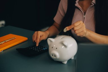 Genç Asyalı kadın emeklilik için para biriktiriyordu. Kumbaradan para biriktiriyordu ve defter, tasarruf konsepti gibi notlar alıyordu..