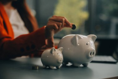 A young girl works at a laptop, writes a business development plan in a notebook, develops a strategy and makes calculations of earned funds. A woman puts her savings in a piggy bank.