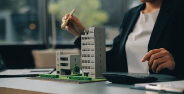 Yakın mesafede emlakçı, küçük ev modelini ve kır evinin planını tutuyor. Gayrimenkul alımı, yeni mülk, mülkiyet, inşaat şirketi müşteriye özel teklifte bulundu, uygun fiyatlı konut kavramı