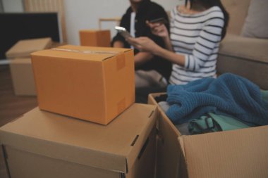 İki Asyalı blogcu, dükkanında canlı yayın yapan videoyu kaydetmek için kameranın önünde kıyafetlerini gösteriyor. Çevrimiçi alışveriş arabası fikri. Evdeki kanepede.