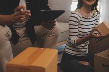 İki Asyalı blogcu, dükkanında canlı yayın yapan videoyu kaydetmek için kameranın önünde kıyafetlerini gösteriyor. Çevrimiçi alışveriş arabası fikri. Evdeki kanepede.