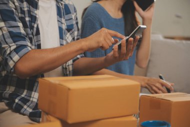 İki Asyalı blogcu, dükkanında canlı yayın yapan videoyu kaydetmek için kameranın önünde kıyafetlerini gösteriyor. Çevrimiçi alışveriş arabası fikri. Evdeki kanepede.