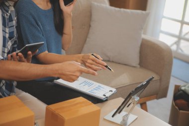 İki Asyalı blogcu, dükkanında canlı yayın yapan videoyu kaydetmek için kameranın önünde kıyafetlerini gösteriyor. Çevrimiçi alışveriş arabası fikri. Evdeki kanepede.