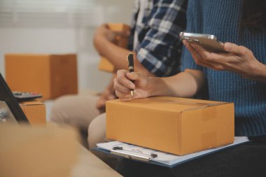 İki Asyalı blogcu, dükkanında canlı yayın yapan videoyu kaydetmek için kameranın önünde kıyafetlerini gösteriyor. Çevrimiçi alışveriş arabası fikri. Evdeki kanepede.