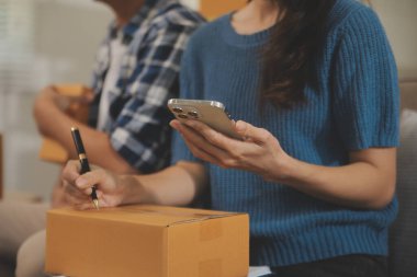 İki Asyalı blogcu, dükkanında canlı yayın yapan videoyu kaydetmek için kameranın önünde kıyafetlerini gösteriyor. Çevrimiçi alışveriş arabası fikri. Evdeki kanepede.