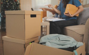 İki Asyalı blogcu, dükkanında canlı yayın yapan videoyu kaydetmek için kameranın önünde kıyafetlerini gösteriyor. Çevrimiçi alışveriş arabası fikri. Evdeki kanepede.