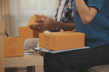 İki Asyalı blogcu, dükkanında canlı yayın yapan videoyu kaydetmek için kameranın önünde kıyafetlerini gösteriyor. Çevrimiçi alışveriş arabası fikri. Evdeki kanepede.