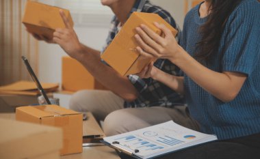 İki Asyalı blogcu, dükkanında canlı yayın yapan videoyu kaydetmek için kameranın önünde kıyafetlerini gösteriyor. Çevrimiçi alışveriş arabası fikri. Evdeki kanepede.