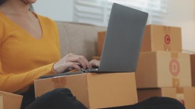 Odasında bir sürü karton kutu olan Asyalı bir kadın. Çevrimiçi ürünler satan genç kadın girişimci, indirme ve çevrimiçi iş aracı 