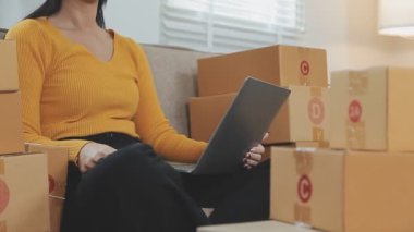 Odasında bir sürü karton kutu olan Asyalı bir kadın. Çevrimiçi ürünler satan genç kadın girişimci, indirme ve çevrimiçi iş aracı 