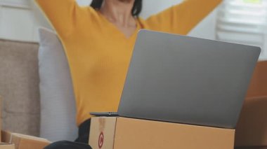 Odasında bir sürü karton kutu olan Asyalı bir kadın. Çevrimiçi ürünler satan genç kadın girişimci, indirme ve çevrimiçi iş aracı 